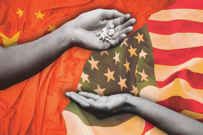 A hand giving pills to another hand with a backdrop of the US and China flags.